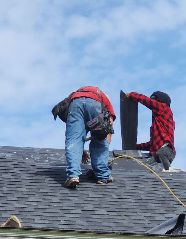 Two roofers working on a shingle roof next to a vent